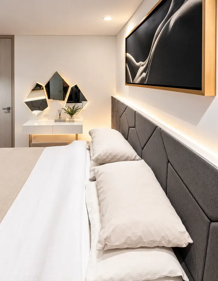 Glamour, Airbnb diseñado por ALUZINA en Medellín: dormitorio con cabecero gris geométrico, luz cálida indirecta y espejos facetados
