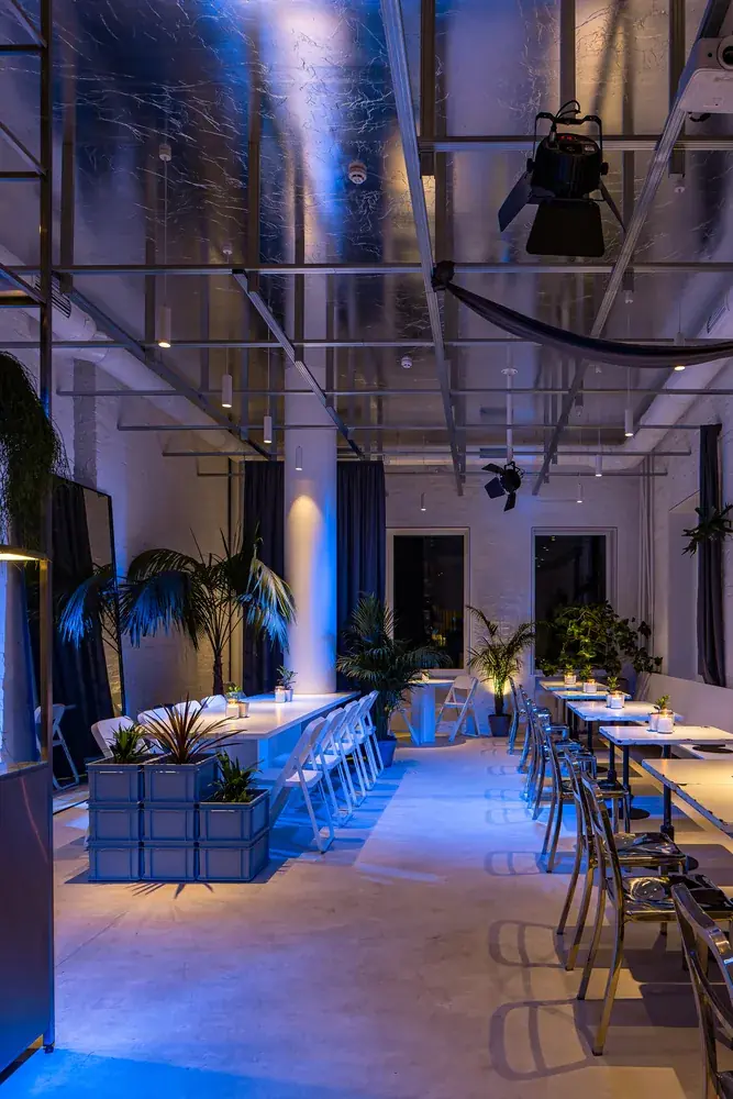 Comedor de un restaurante diseñado por ALUZINA en Medellín de noche, con iluminación azul, palmeras y mesas blancas